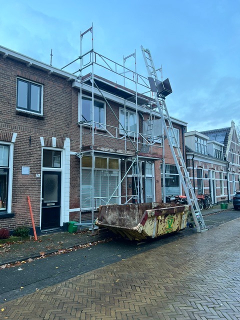 Woninggevel met steiger, ladder en afvalcontainer tijdens voorbereidende sloopwerkzaamheden